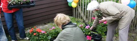 Twee buurtbewoners zetten bloemen in de border langs een
                              voortuin tijdens de wijkschoonmaakdag.