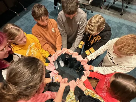 Een groep jongeren legt hun handen bij elkaar in een cirkel,
                              van bovenaf gezien.