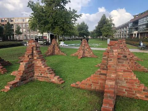Drie piramidevormige bouwwerken van losse baksteentjes op een
                              grasveld tussen de flats.