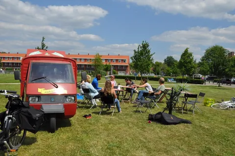 Een mobiel terras met stoelen op een grasveld, met bewoners die
                              in de zon zitten.