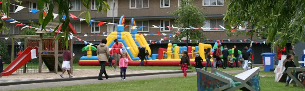 Kinderen en ouders op een grasveld met slingers, luchtkussens en een glijbaan
              tijdens het multiculti-straatfeest aan de Meridiaan.
