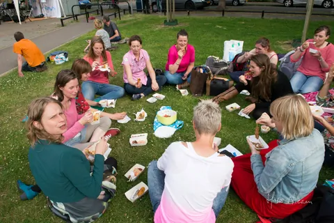 Gezinnen zitten met kleedjes en spelletjes op het gras tijdens
                              Proef Kruiskamp.