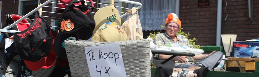 Uitgestalde spulletjes met een handgeschreven bordje 'te koop' op een kleedje
              tijdens de rommelroute.