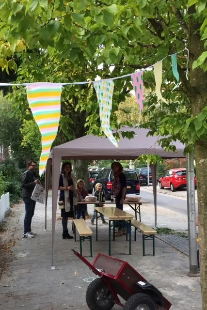 Gekleurde vlaggetjes hangen boven een partytent en een kruiwagen
                          tijdens het straatfeest in de Trompstraat.
